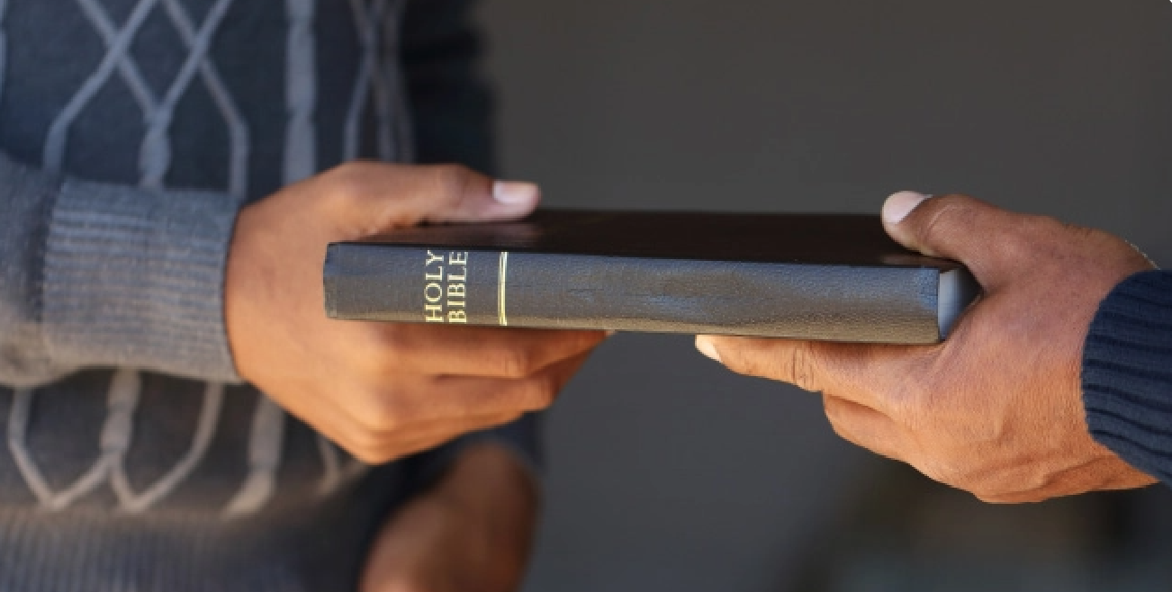 Hand giving Bible to another hand